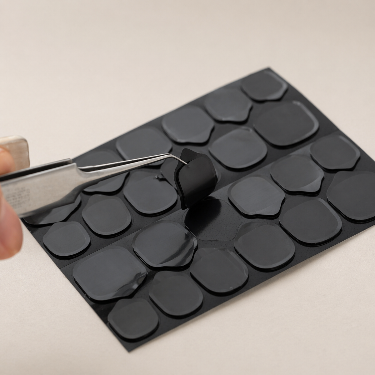 ピンセットで黒いネイル粘着グミをシートから剥がしている様子
