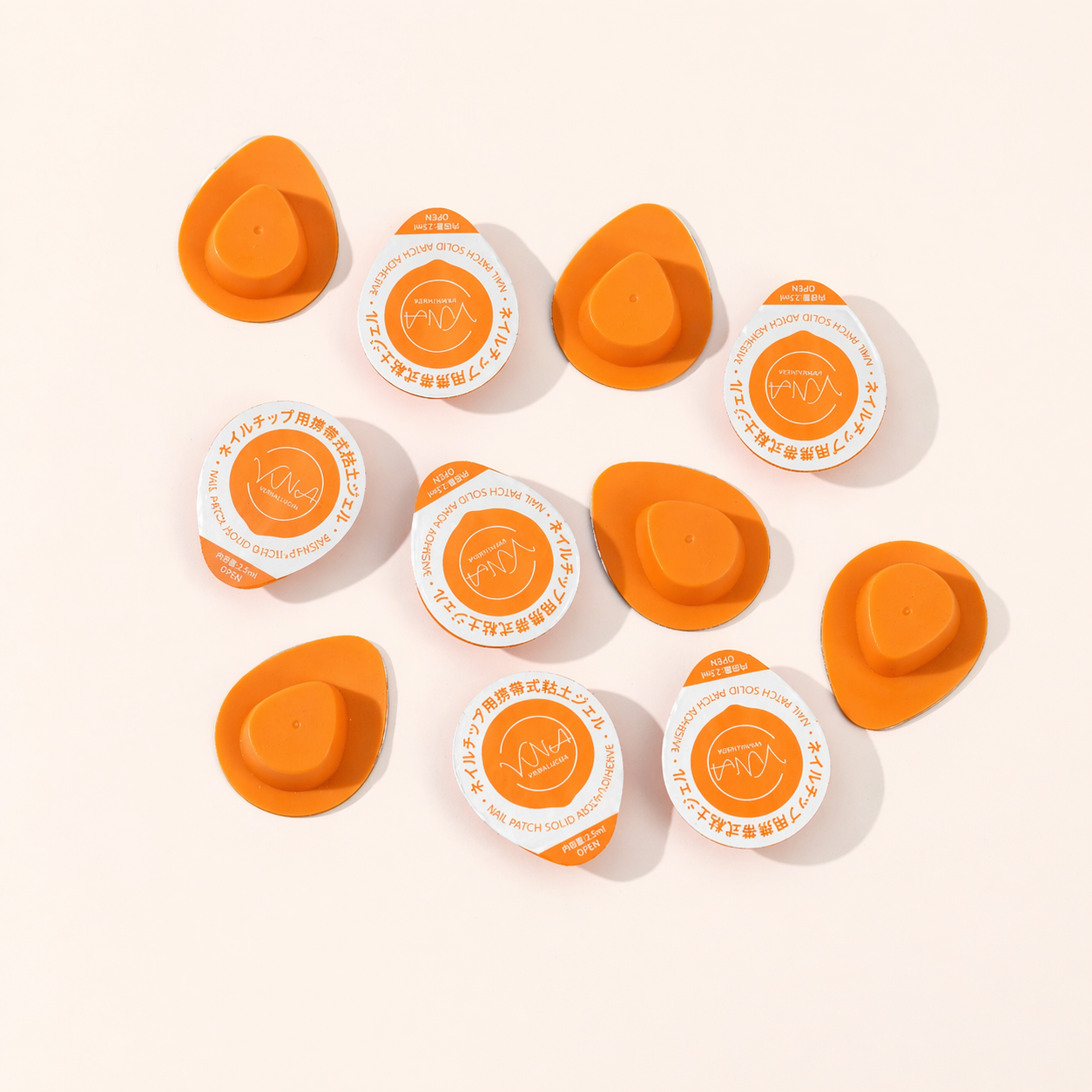 Orange portable nail adhesive gel patches arranged on a white background